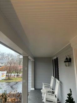 Covered porch with white rocking chairs, light gray siding, and a black light fixture.