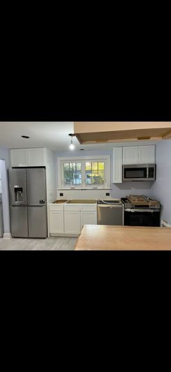A renovated kitchen with white cabinets, stainless steel appliances, and a wooden countertop.