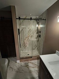 Bathroom with marble tile shower, glass door, dark fixtures, and vanity.