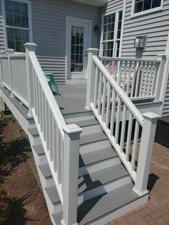 White railing surrounds gray composite deck with stairs leading down to a brick patio.