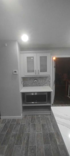 A kitchen with white cabinets, a microwave, and gray tiled flooring.