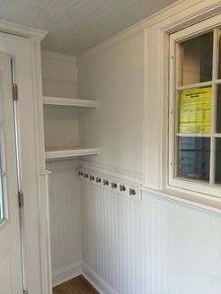 White entryway with shelves, coat hooks, and a window.