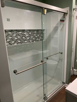Glass shower enclosure with white walls, mosaic tile, and a grab bar.