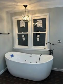 Modern bathroom with a white freestanding tub under a window with a chandelier and dark fixtures.