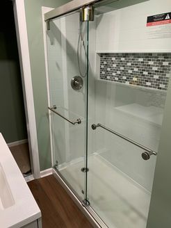 Shower with clear glass doors, white walls, and a tiled niche. Features include grab bars and a silver showerhead.