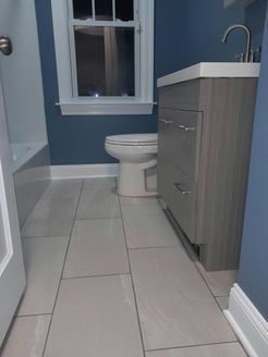 Bathroom with gray vanity, toilet, and light-colored tiled floor; blue walls; white trim.