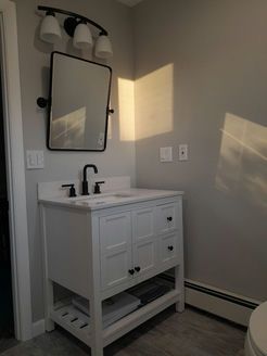 White bathroom vanity with black fixtures, mirror, and light, against gray walls.