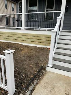 A house front with a porch, steps, and new wooden siding, in progress with bare dirt.
