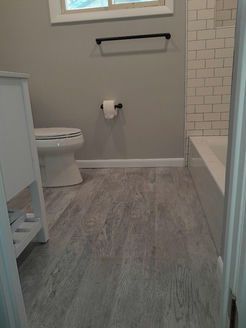 Bathroom with gray wood-look flooring, white toilet, gray walls, and white subway tile in the shower.