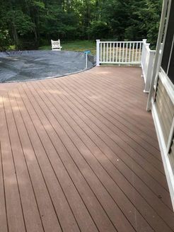 Brown composite deck with white railing, overlooking a pool covered with a black tarp.