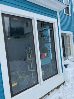 Two large windows with dark frames on a blue building, snow on the ground.
