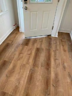 Wooden-look flooring leading to a white door. The floor has a medium brown tone.