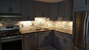 Gray kitchen with cabinets, backsplash, and appliances, including a stove, dishwasher, and refrigerator.