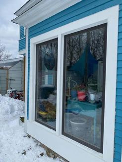 Two dark-framed windows in a blue house reflect a snowy scene.
