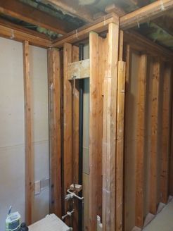 Wooden studs framing a partial wall in a basement, pipes and electrical outlets are visible.