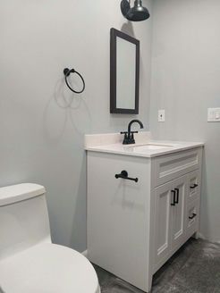 Small white bathroom with a toilet, sink, mirror, and black fixtures.