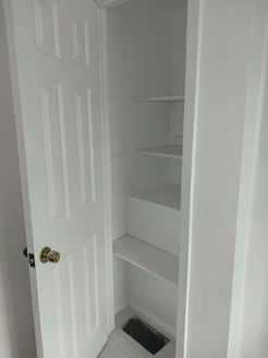 White pantry with shelves, door open. Air vent at the bottom.