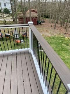 Deck with gray boards, white railing posts, and black spindles. Brown handrail with a natural outdoor setting.