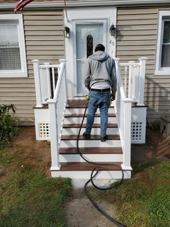 Person walking up wooden stairs to a house with white railing. A black hose runs down the stairs.