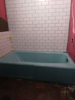 A blue bathtub in a bathroom with white tiled walls and pink curtain.