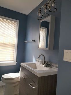 Bathroom with blue walls, a white sink and toilet, and a window with blinds.