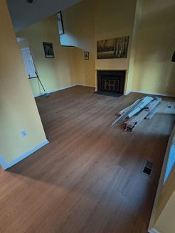 Living room with laminate flooring, yellow walls, fireplace, and exposed baseboards.