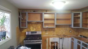 Kitchen renovation in progress: upper cabinets, stove, and exposed wall with damaged wallpaper.