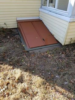 Brown metal bulkhead doors against a yellow house wall.