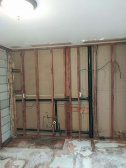 Interior wall under construction with exposed wooden frame, plumbing, and electrical wiring.