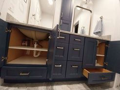 Navy blue bathroom vanity with open doors and drawers; light grey countertop, white sink.