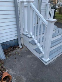 White and gray outdoor stairs with a matching handrail next to a white house with a gray downspout.