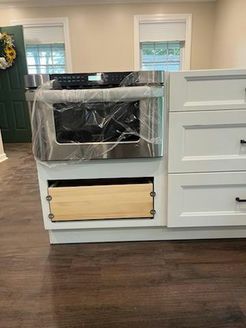 New kitchen cabinet with installed stainless steel oven, a drawer, and white cabinets.