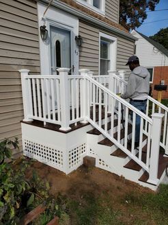 Person standing on the steps of a white porch with railings. The house is beige with a white door.