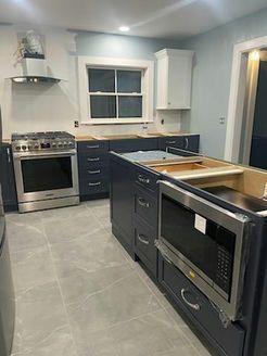 Newly renovated kitchen with dark blue cabinets, stainless steel appliances, and gray tile floor.