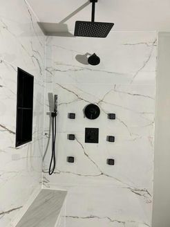Modern shower with white marble-look tile, black fixtures, multiple jets, and a built-in bench.