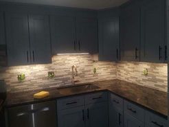 Modern kitchen with blue cabinets, a tiled backsplash, and dark countertops.