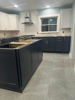 Modern kitchen renovation with dark blue base cabinets, white upper cabinets, and gray tile floor.