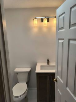 Bathroom with a toilet, vanity, and light fixture. Door is partially open.