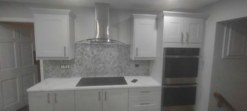 Kitchen with white cabinets, stainless steel range hood, granite backsplash, and black cooktop.