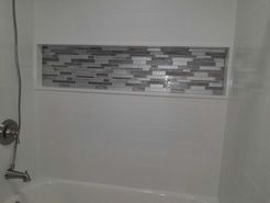 White tiled bathroom with a tiled niche containing mosaic tiles. Showerhead and faucet are visible.