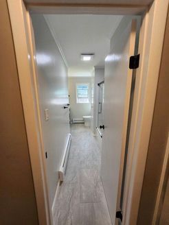Hallway leading to bathroom. Gray walls, light gray tile floor, white door frames, and a toilet visible.