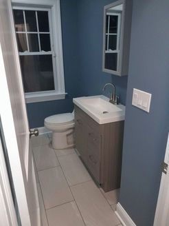 Small bathroom with blue walls, white fixtures, and a gray vanity.