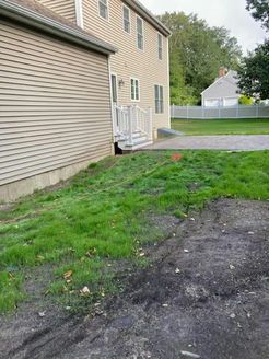 A house with a side yard covered in grass, dirt, and a driveway.