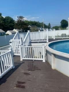 Above-ground pool with white railing, wooden deck, and blue water, on a sunny day.