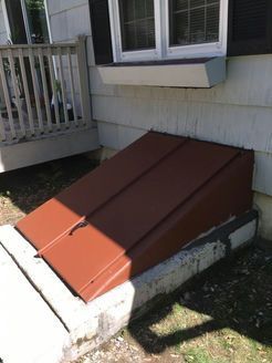 Brown metal cellar door built into a concrete foundation next to a porch.