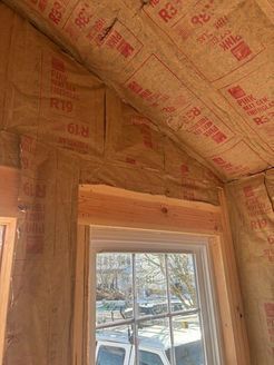 Interior of a building under construction, with exposed insulation in the walls and ceiling, and a framed window.