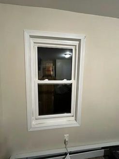 White-framed double-hung window on a beige wall, reflecting interior with light and dark areas.
