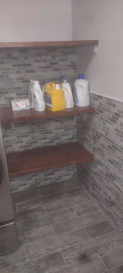 Laundry room with wood shelves holding cleaning supplies against tiled wall.