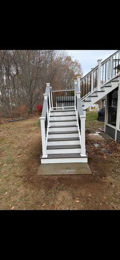 A wooden staircase with gray steps and white railings leads up from a brown yard.