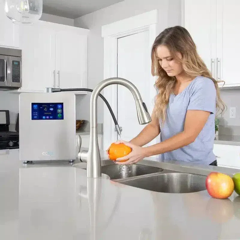 Woman washing produce at kitchen sink, near a water purification system.